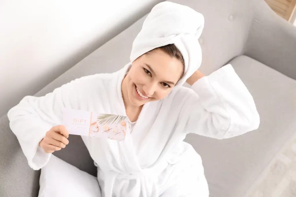 Femme en peignoir souriante tenant une carte cadeau massage